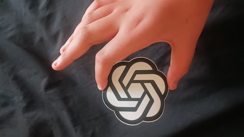A person holding a small model of the OpenAI logo